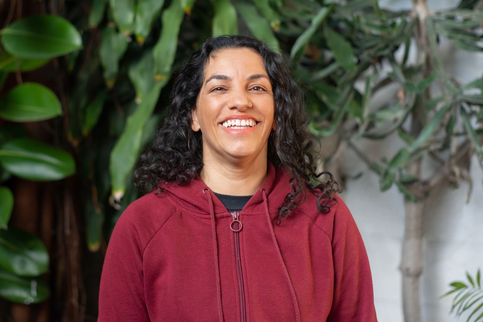 A woman with dark curls smiling among sunlit plants